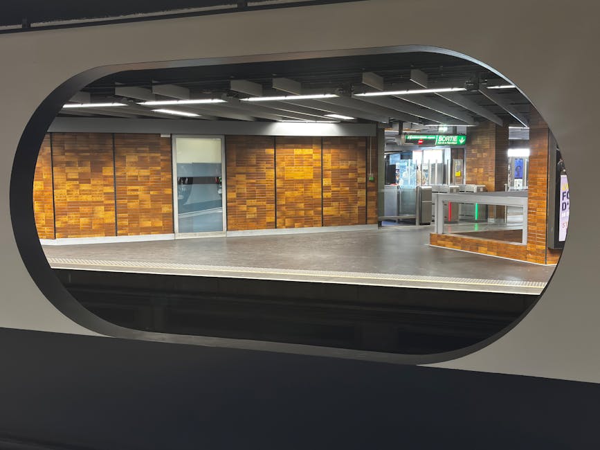 Enfield Town train station platform with a row of brick-built waiting areas featuring white-framed windows along the left side, and a covered walkway with support columns on the right. The platform su